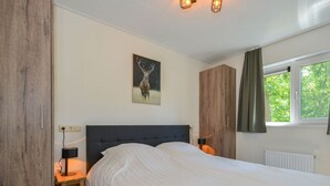 A bedroom with a large bed, a nightstand with a lamp, a wooden wardrobe, and a painting of a deer on the wall. - Pavilion 6 People With Storage Space (Zorgvlied)