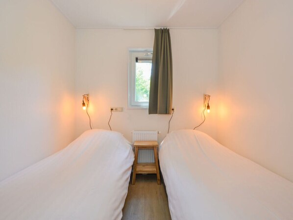 A small, clean room with two single beds, a window with a curtain, and wall-mounted reading lights.