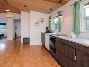 A modern kitchen with wooden flooring, a dishwasher, and a window with green curtains. - 4 Star Holiday Home in Ansager (Ansager)