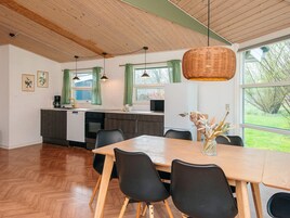 Una cocina moderna con armarios de madera, una mesa de comedor con sillas y ventanas grandes con cortinas.