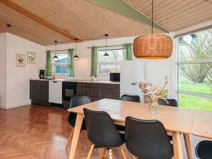 A modern kitchen with a dining area, wooden flooring, and large windows.