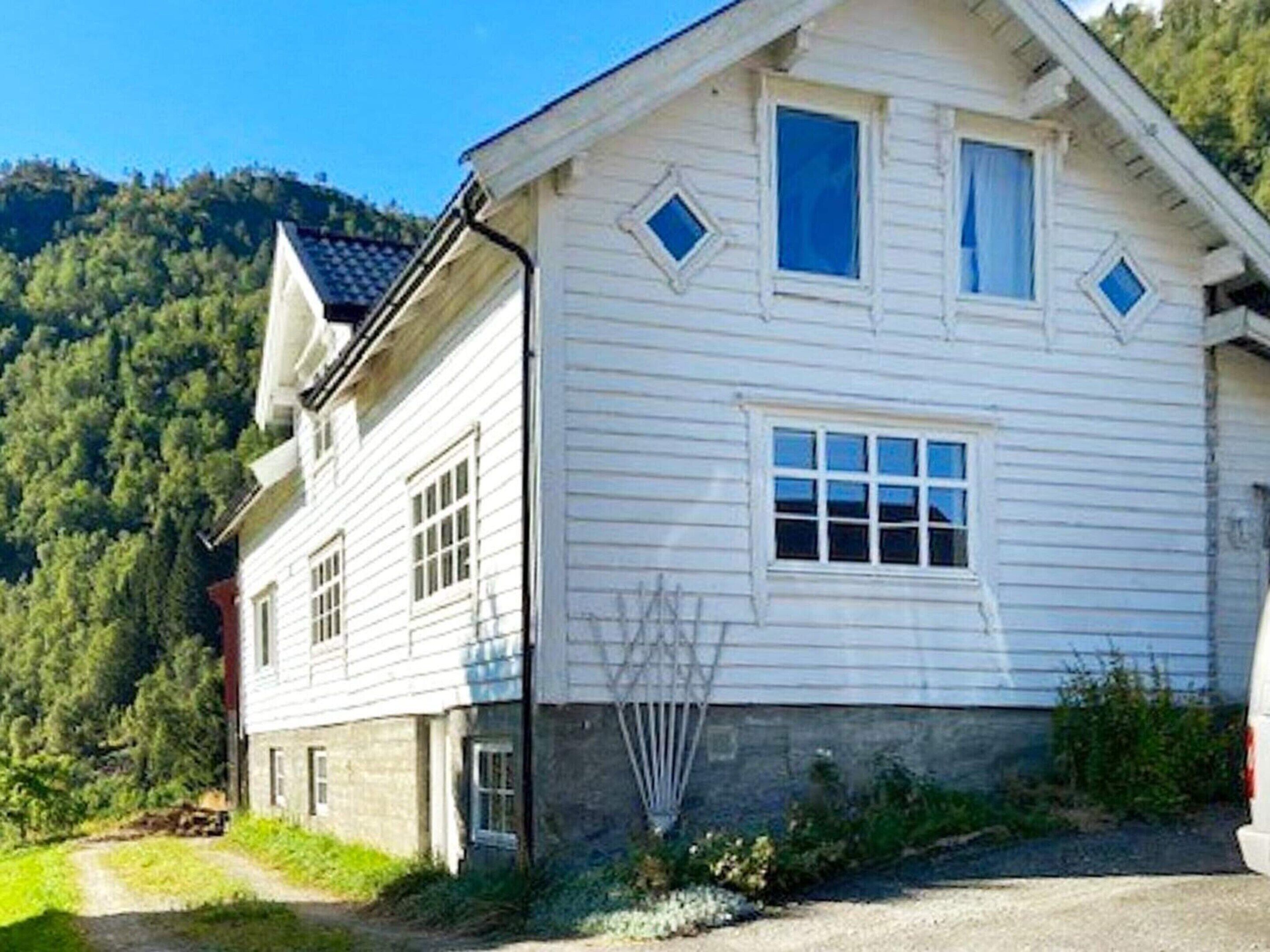 Una casa de madera blanca con techo pronunciado, varias ventanas y un pequeño porche.