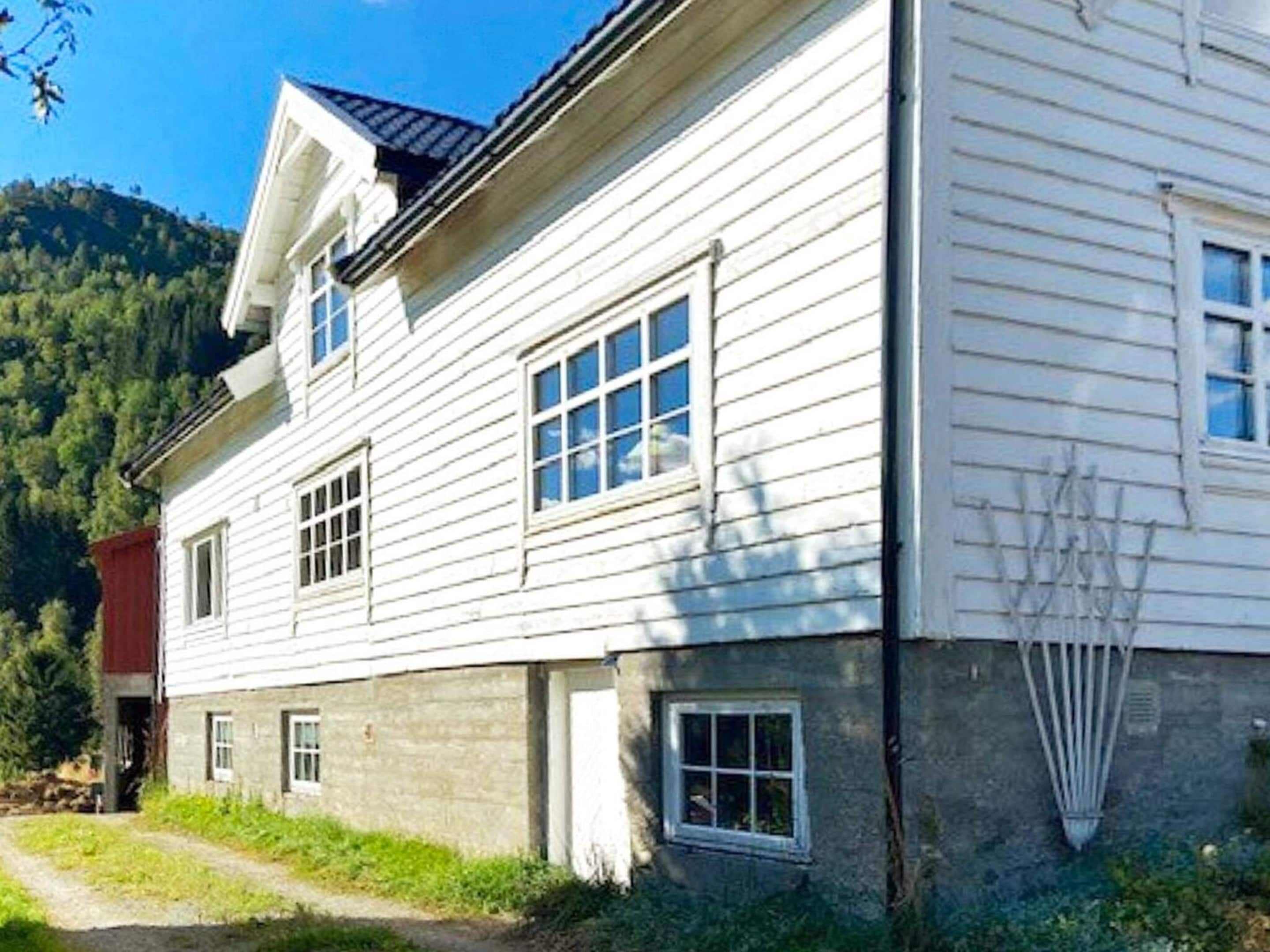 Una casa de madera blanca de dos pisos con techo inclinado, una chimenea visible y un pequeño porche.