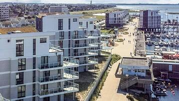 Un edificio moderno de varios pisos con balcones, un puerto deportivo con barcos y vistas al mar.