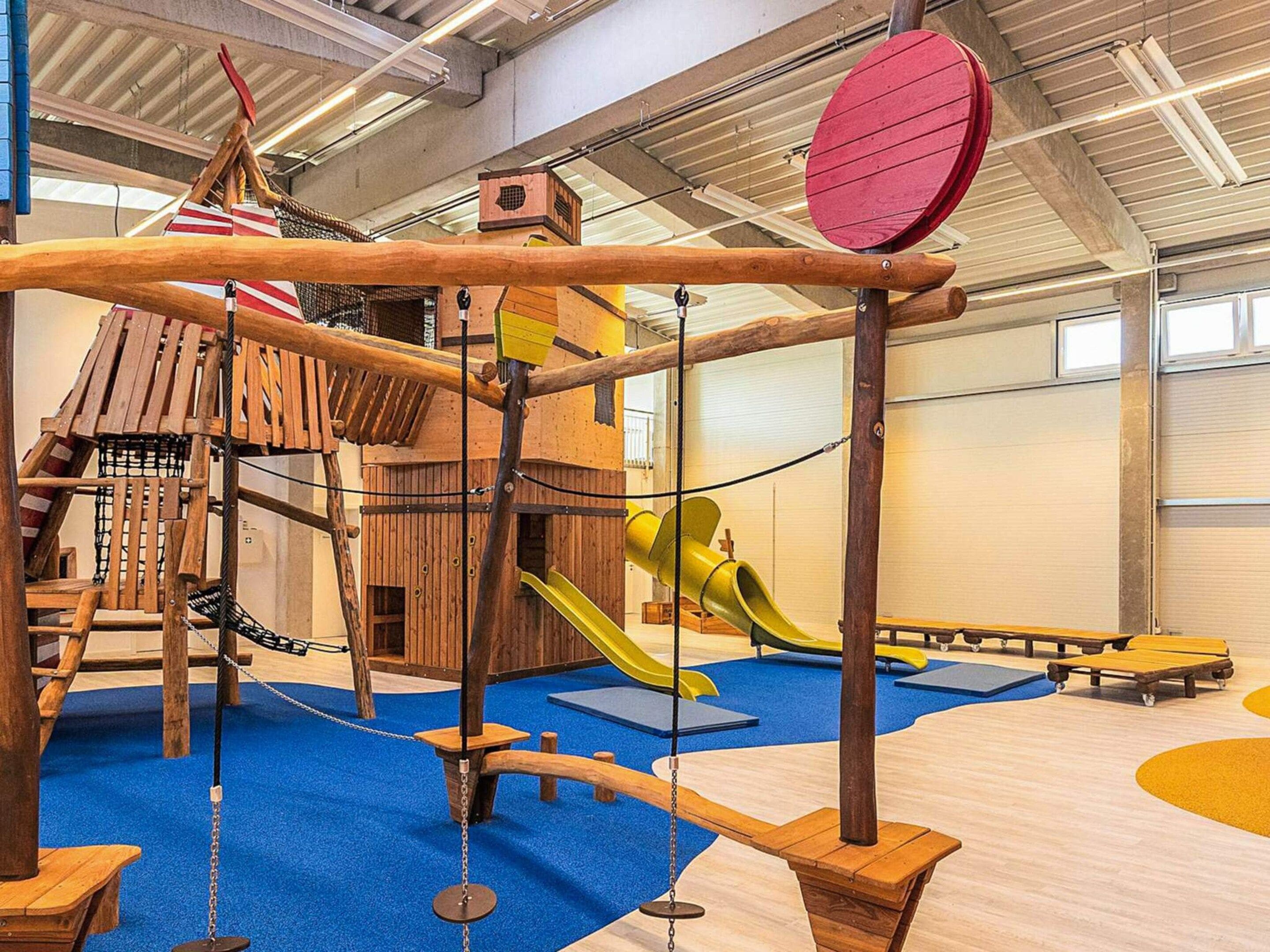 A play area with a wooden climbing structure, slides, and a rope bridge.