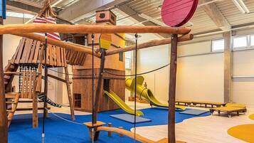 Zona de juegos con una estructura de madera para escalar, toboganes y un puente colgante.