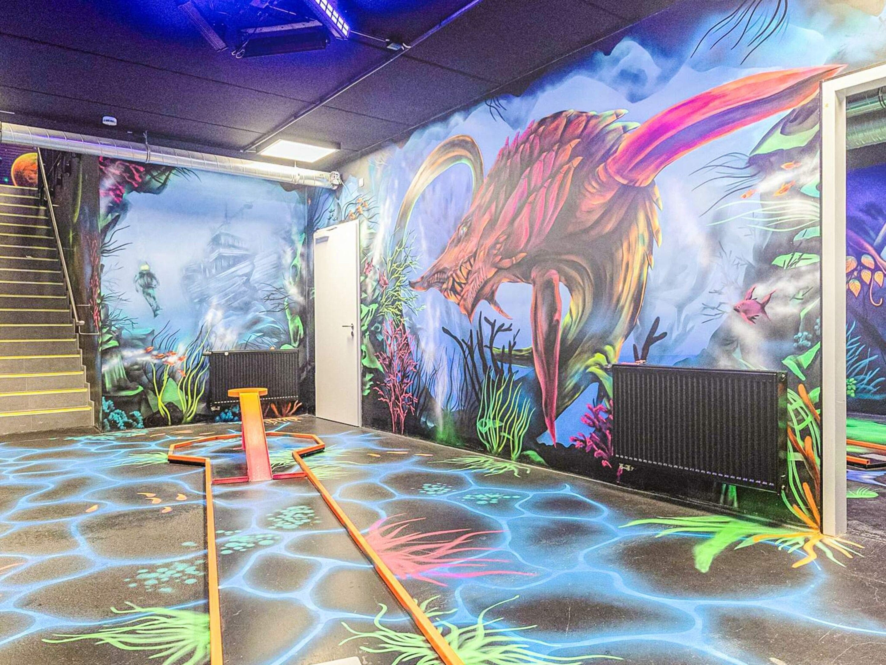 Un espacio interior con un mural de una escena prehistórica, que incluye un dinosaurio grande y plantas de la época.