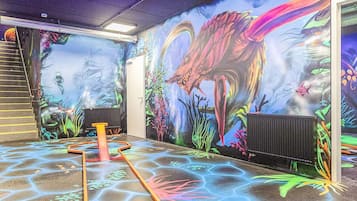 Un espacio interior con un mural de una escena prehistórica, que incluye un dinosaurio grande y plantas de la época.