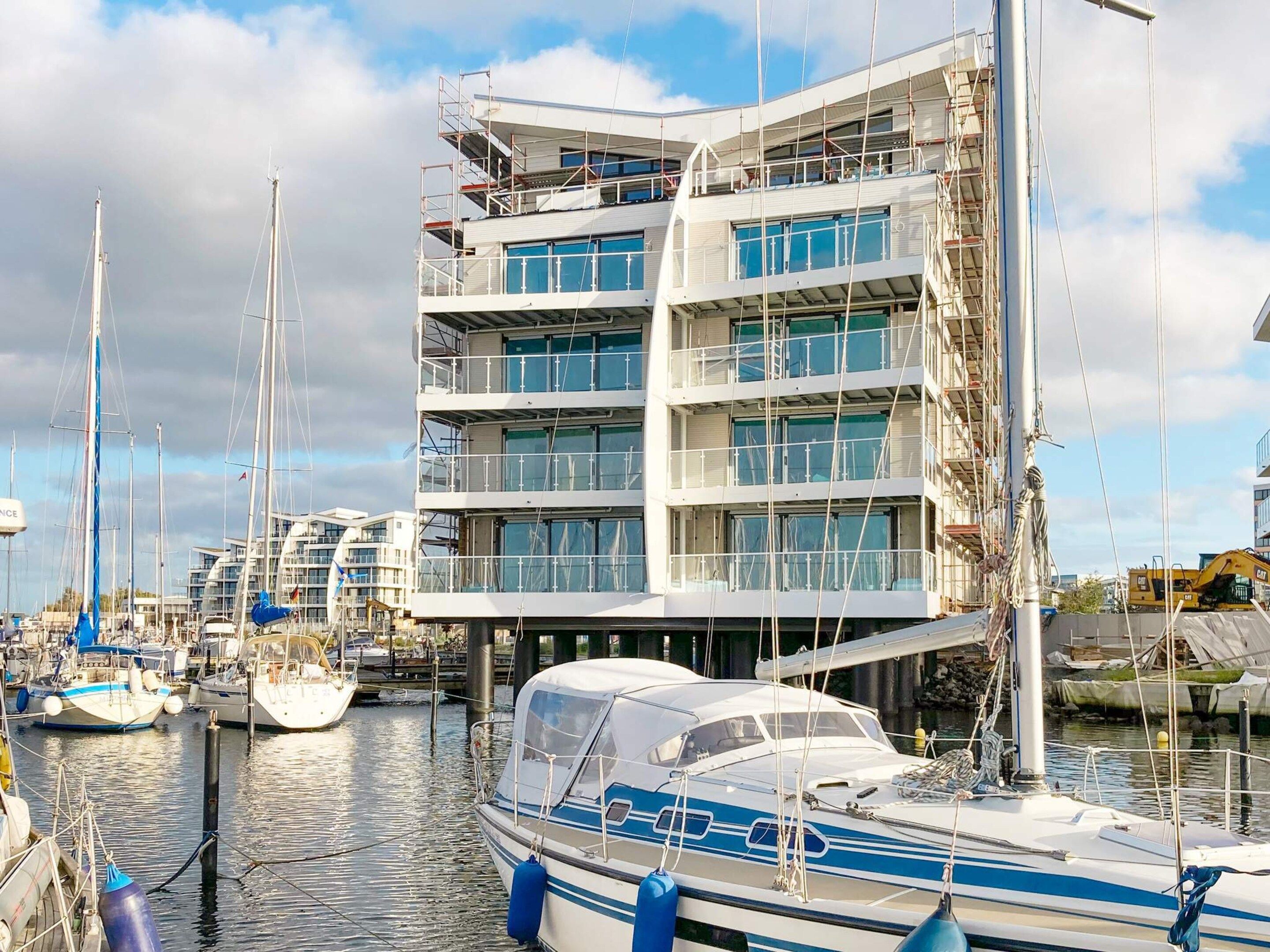 Un immeuble à plusieurs étages doté de balcons, une marina avec des bateaux et du matériel de construction.
