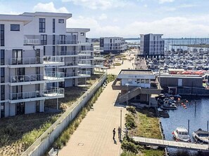 A coastal residential area with modern buildings, a marina, and a pedestrian walkway. - 5 Star Holiday Home in Wendtorf (Wendtorf)