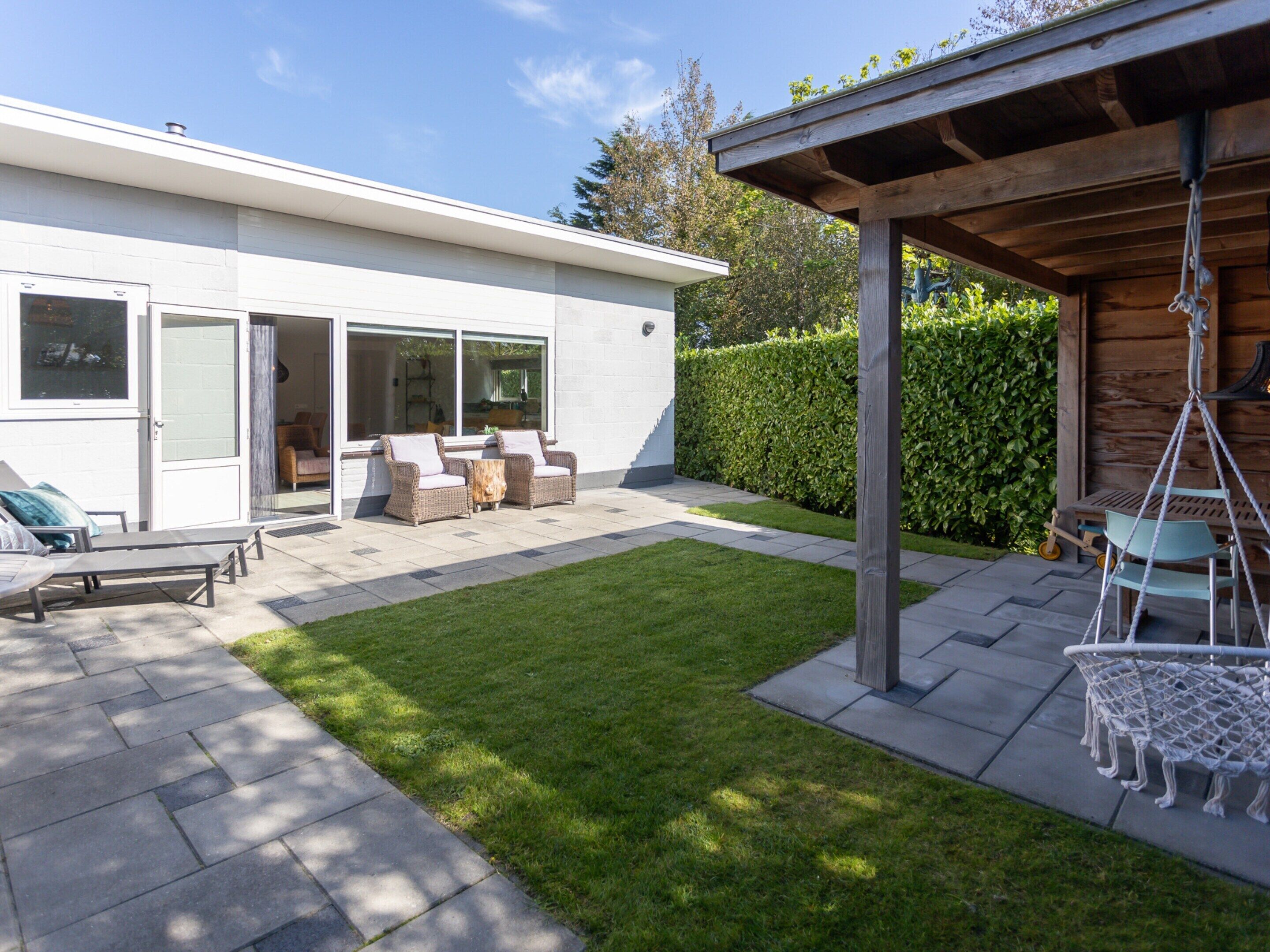 A modern house with a patio, outdoor furniture, and a swing chair.