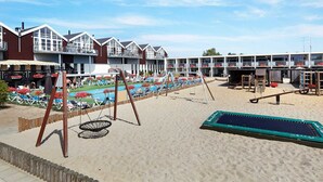 A beachside hotel with multiple buildings, a swimming pool, sun loungers, and a swing set. - 4 Person Holiday Home on Holiday Park in Glesborg (Glesborg)