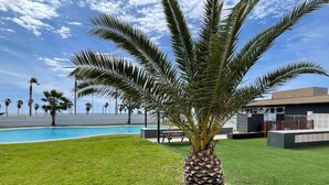 Ein Poolbereich mit einer Palme, einem modernen Gebäude und Blick auf den Ozean.