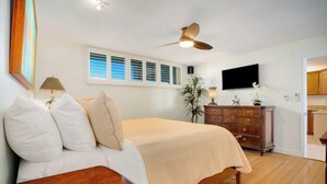 A bedroom with a bed, wooden dresser, ceiling fan, and a TV mounted on the wall.