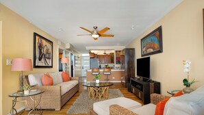 A spacious living area with wicker furniture, a ceiling fan, a television, and artwork on the walls.