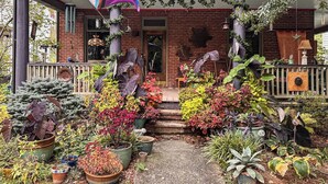 Une maison en briques avec un porche décoré de plantes et orné d’un drapeau arc-en-ciel.