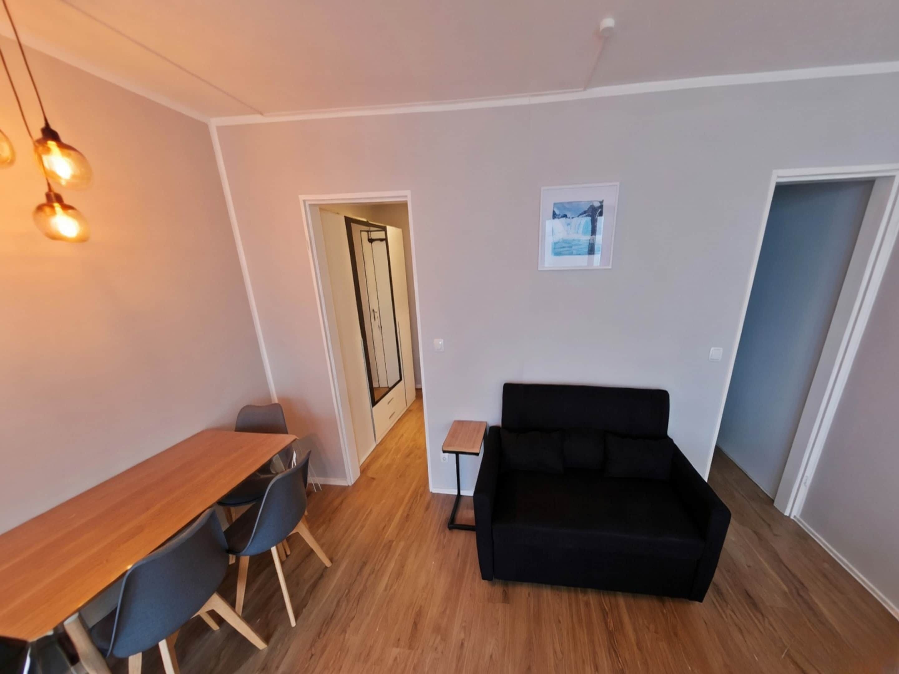 Un salon moderne avec une table à manger en bois, un canapé noir et une petite table d’appoint.