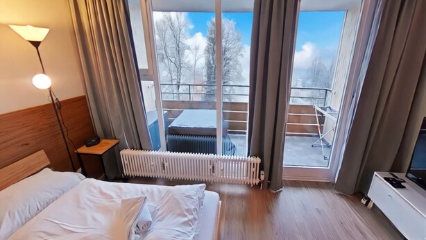 A hotel room with a bed, a desk with a lamp, a radiator, and a TV. - Appartement Serges mit Pool und Sauna in Freyung (Freyung)
