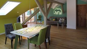 A dining area with a table, chairs, and a view of a green wall with a lighted animal silhouette. - Villa Carefree Suite (Grassau)