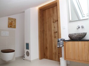 A modern bathroom with a wooden door, a stone basin sink, and a toilet with a brown seat. - Villa Carefree Suite (Grassau)