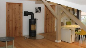 A modern loft bedroom with a built-in wood-burning stove, a small dining table, and a staircase. - Villa Carefree Suite (Grassau)