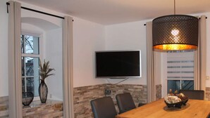 A dining area with a wooden table, six chairs, a TV mounted on the wall, and a decorative lamp.