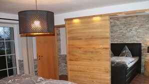 A bedroom with a bed, a wooden wardrobe, and a stone wall.