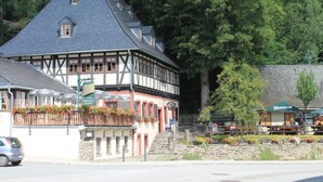 A traditional half-timbered building with a steeply pitched roof, a stone foundation, and a small balcony with flower boxes.