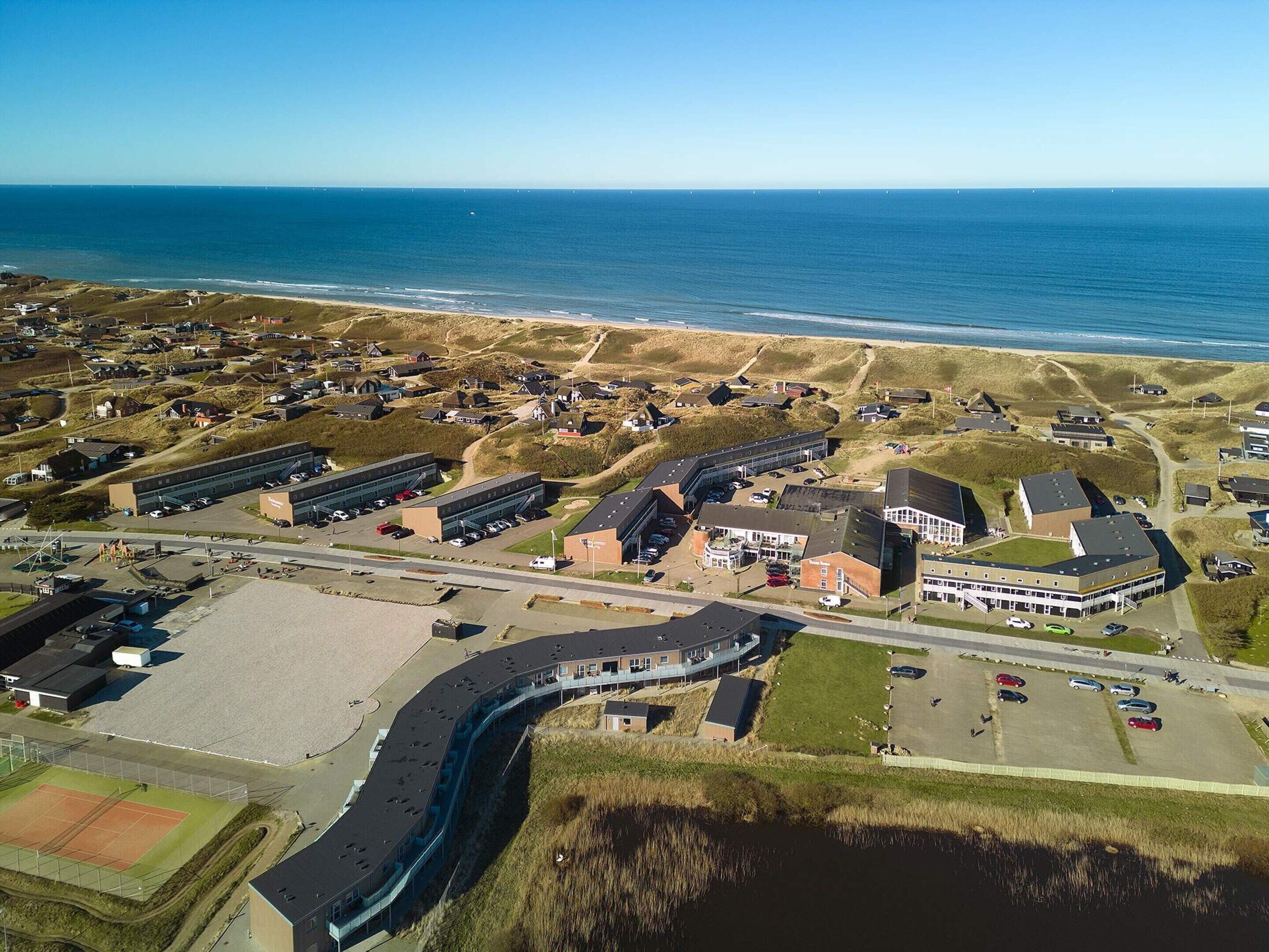An aerial view of a coastal area with buildings, a tennis court, and a beach.