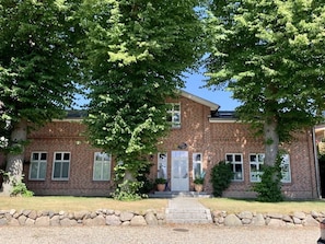 A brick building with a central entrance, windows on both sides, and a stone border in front. - Kleine Freiheit Fehmarn (Fehmarn)