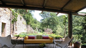An outdoor seating area with a yellow sofa, two white folding chairs, and a table with books and a vase of flowers. - Villa With Pool in Sarteano (Chianciano Terme)