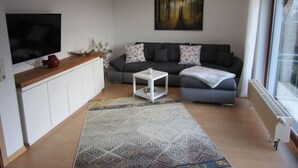 A modern living room with a grey sofa, a white coffee table, and a flat-screen TV. - Holiday Apartment Hammann (Sietow)