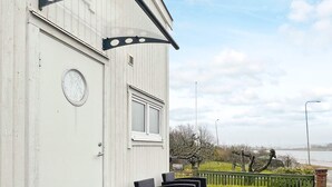 En hvid bygning med en dør, et vindue og en lille balkon med sorte stole.