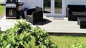 En udendørs terrasse med grill, fletmøbler og en skydedør til et overdækket område.