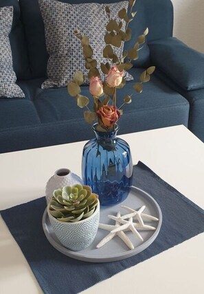 Un vase bleu contenant des roses et une plante succulente, le tout posé sur un plateau, est placé sur une table blanche devant un canapé bleu.