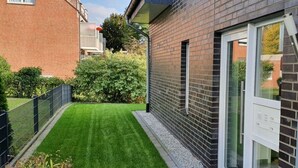 A modern building with a brick exterior, a well-maintained lawn, and a metal fence. - Holiday Apartment on the Lindenallee (Bad Rothenfelde)