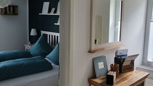 A bedroom with a bed, a nightstand, a lamp, a dresser with a mirror, and a window with blinds. - Holiday Apartment on the Lindenallee (Bad Rothenfelde)
