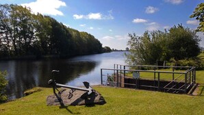 A riverside view with a bicycle parked on a rock, a metal railing, and a grassy area. - Pumpe an der Eider (Dellstedt)