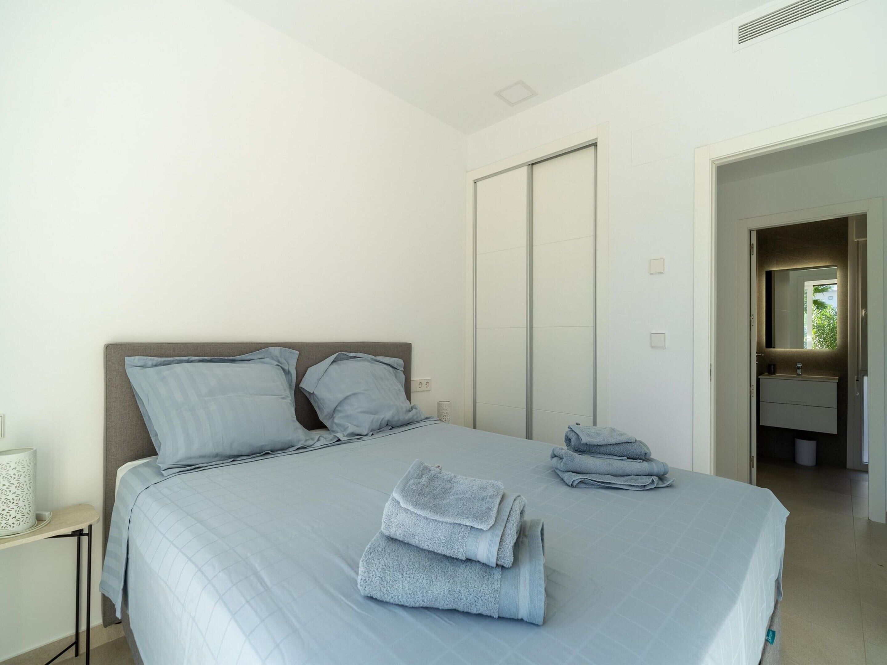 A bedroom with a bed, pillows, a mirror, and a bathroom visible through an open door.