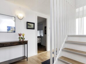 Un pasillo con una consola de madera, una lámpara de pared y un cuadro enmarcado. Una escalera de madera conduce a otra habitación.