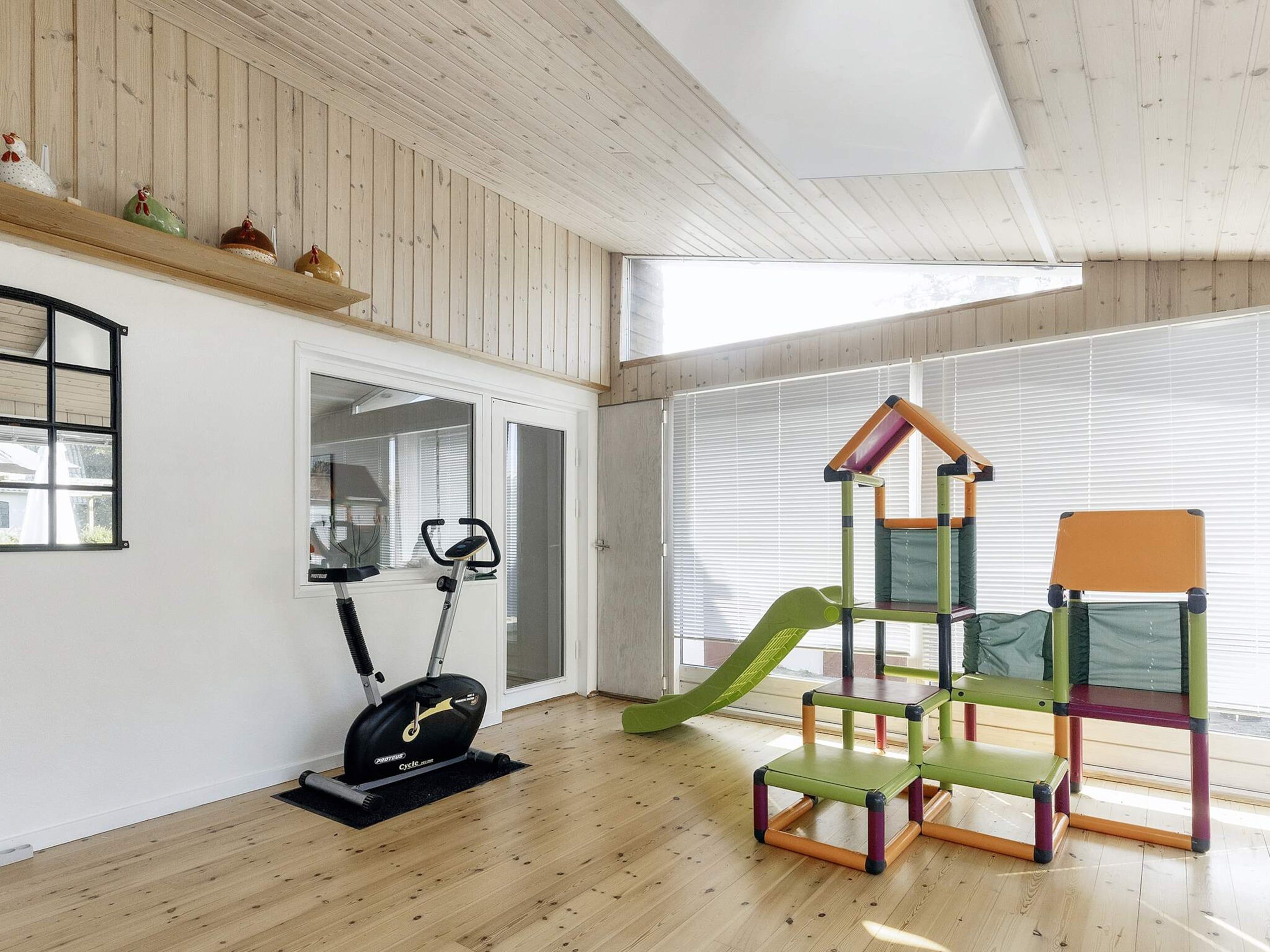 A room with a wooden floor, a stationary bike, a green slide, and colorful chairs.