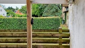 A wooden staircase leading to a building with a hedge in the background. - 8 Person Holiday Home in Nykobing F (Nykøbing Falster)
