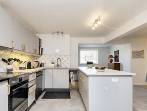 Una cocina moderna con armarios blancos, horno empotrado, pileta y una pequeña isla con un bol de frutas.