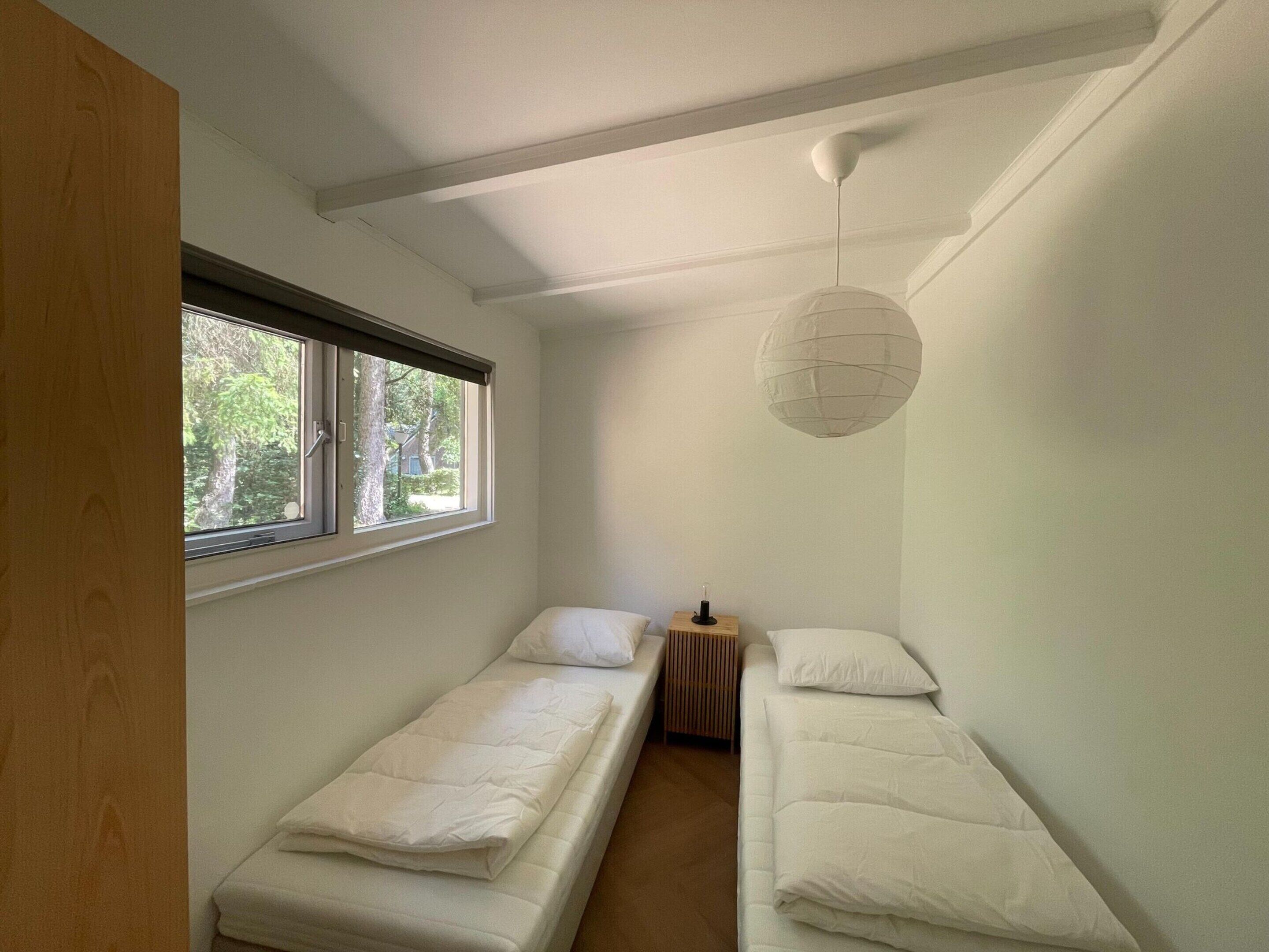 Une petite chambre individuelle avec deux lits simples, une fenêtre et un luminaire suspendu.