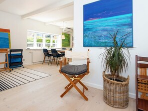 A room with a large window, a painting, a chair, a plant, and a wicker basket. - 6 Person Holiday Home in Ringkobing (Ringkobing)