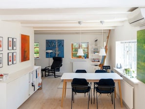 En matplats med ett vitt bord och fyra stolar, en svart stol, ett element och ett fönster med utsikt över grönområden.