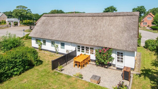 A thatched-roof house with a paved patio, a wooden table and chairs, and a small garden.