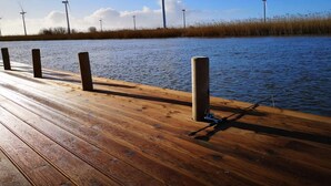 A wooden dock extending over a calm body of water with wind turbines in the background.