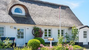 A traditional thatched-roof house with a small circular window, a mailbox, and a bench outside.