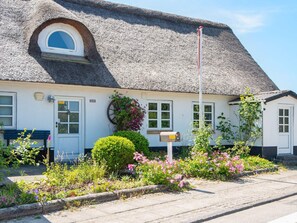 Ett traditionellt hus med halmtak, ett litet runt fönster, en brevlåda och en bänk utanför.